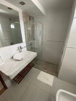 A modern bathroom with a glass-enclosed shower, a white sink with a marble countertop, and a large mirror.