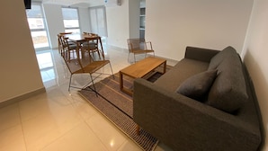 A modern living room with a sofa, coffee table, and dining area with chairs. - HOMEFULL  APARTAMENTOS (Salta)