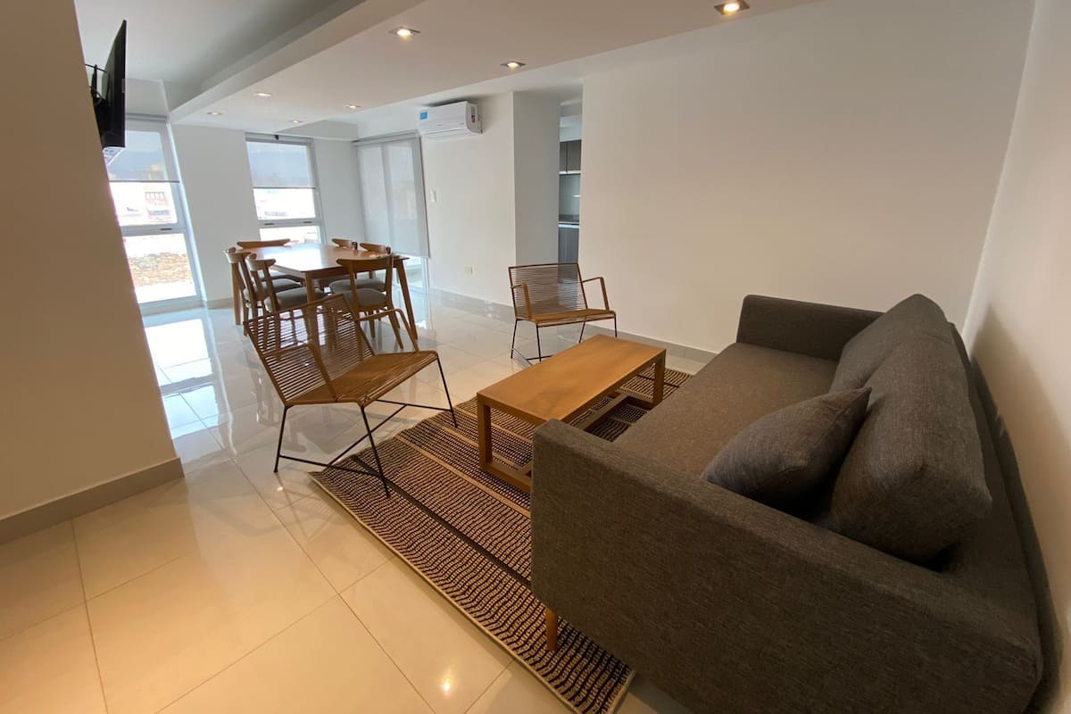 A modern living room with a sofa, coffee table, and dining area with chairs.