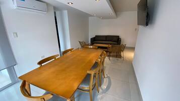 A modern dining area with a wooden table and chairs, a sofa, and a flat-screen TV mounted on the wall.