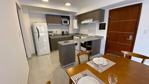 A compact kitchen with modern appliances, a dining area with a wooden table, and a separate dining room. - HOMEFULL  APARTAMENTOS (Salta)