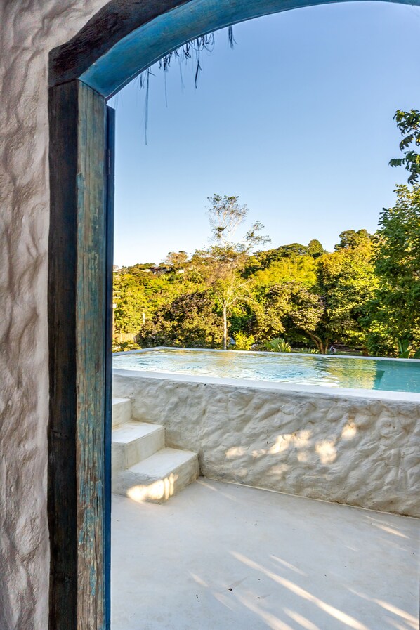 A view of a swimming pool with steps leading up to it, surrounded by a stone wall and trees in the background. - Vila Rudá (Porto Seguro)