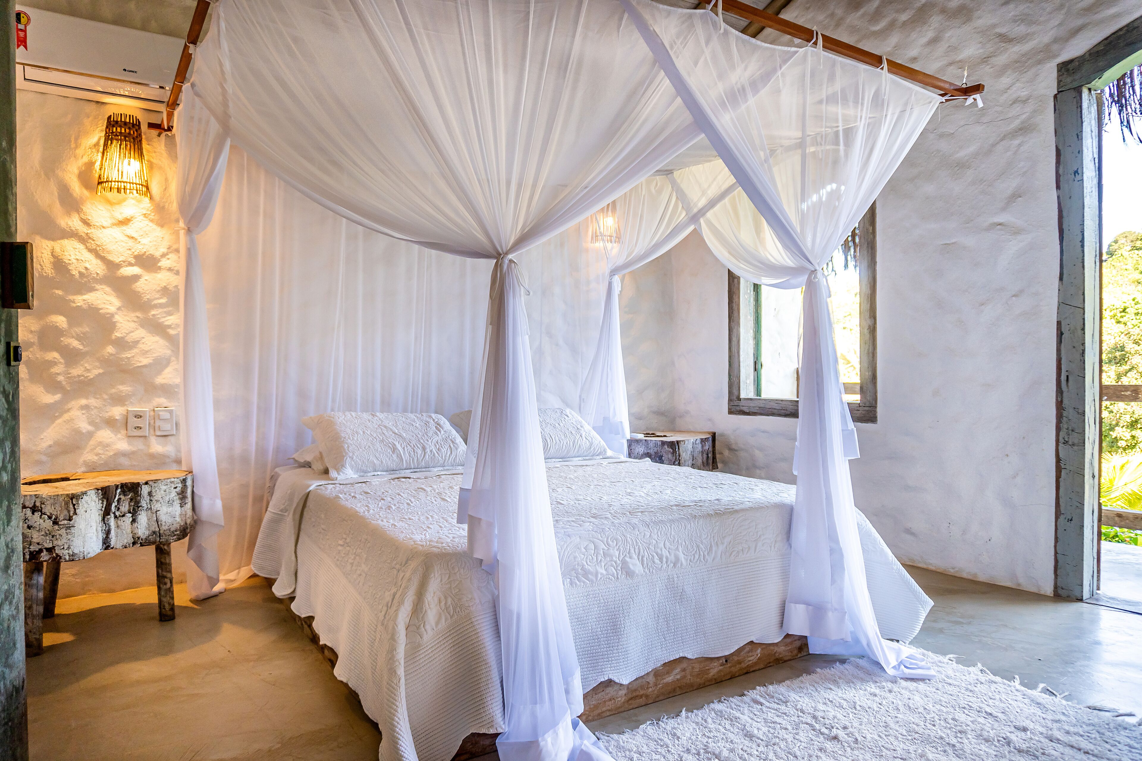 Une chambre à coucher avec un lit à baldaquin, du linge de lit blanc, une table de chevet en bois et une lampe fixée au mur.