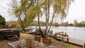 A wooden deck with a table and chairs, surrounded by trees and a body of water. - Avocet Lodge (Lincoln)