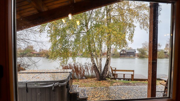 A view from a window overlooking a lake with a wooden dock, a bench, and a hot tub. - Avocet Lodge (Lincoln)