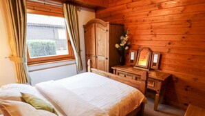 A wooden cabin bedroom with a bed, dresser, and a mirror. - Avocet Lodge (Lincoln)