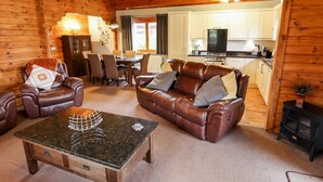 A cozy log cabin interior with a leather sofa, a dining table, and a kitchen area. - Avocet Lodge (Lincoln)
