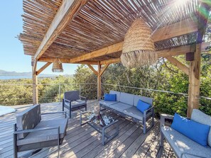 A wooden deck with a thatched roof, outdoor seating, and a view of the landscape.