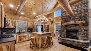 A rustic cabin interior with a stone fireplace, wooden bar, and a large window. - Cabin In the Pines, On Snowmobile Trail (Boonville)
