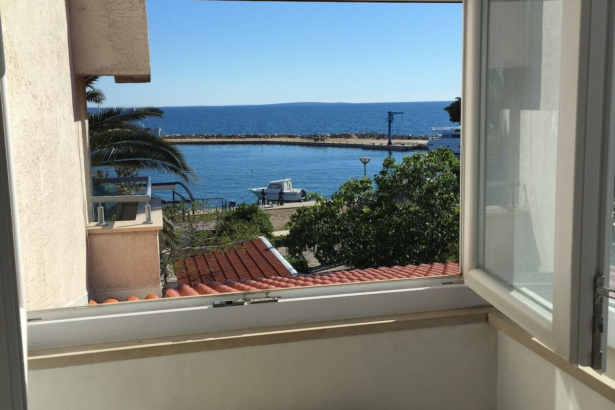 A balcony with a view of the sea, a small table, and a chair.