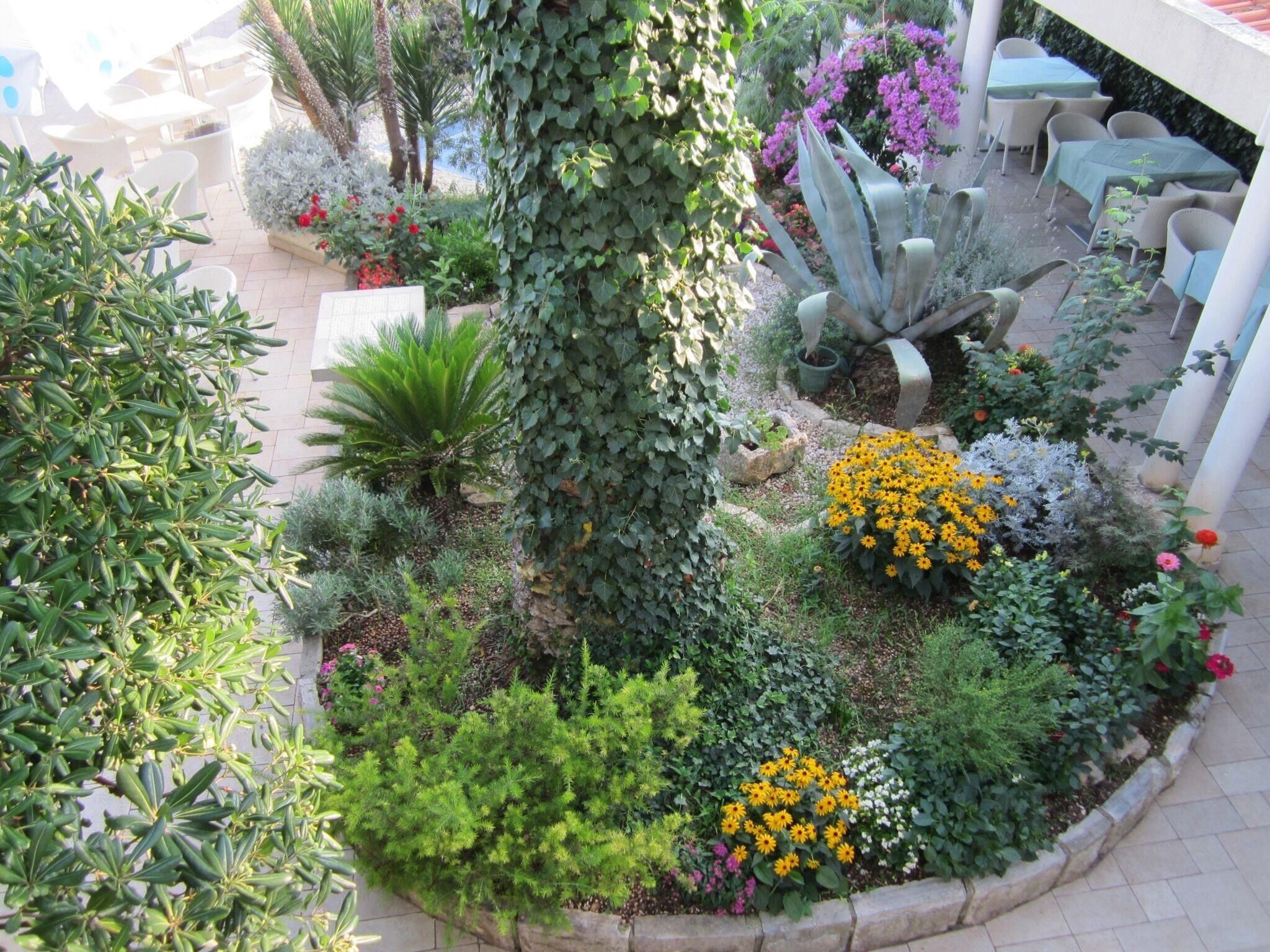 A garden with various plants and flowers, a seating area with tables and chairs, and a pergola structure.