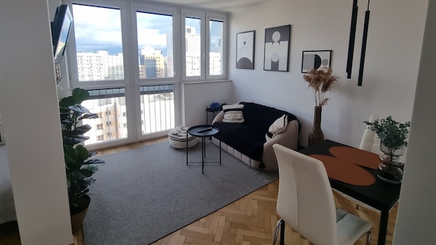 En moderne stue med sofa, spisebord og stort vindue med udsigt over byen.