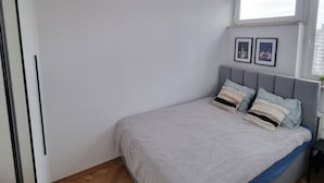 Et soveværelse med seng, trægulv, hvide vægge, et vindue og en loftslampe.