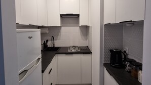 Et lille køkken med hvide skabe, en sort bordplade, en indbygget komfur og en kaffemaskine.