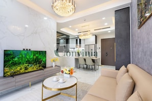 A modern living room with a large flat-screen TV, a round coffee table, a beige sofa, and a chandelier. - Midtown The Peak By Dhome (Ho Chi Minh City)
