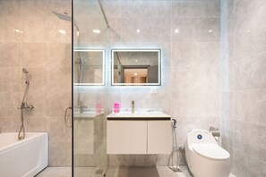 A modern bathroom with a glass shower enclosure, a white vanity with a mirror, and a toilet. - Midtown The Peak By Dhome (Ho Chi Minh City)