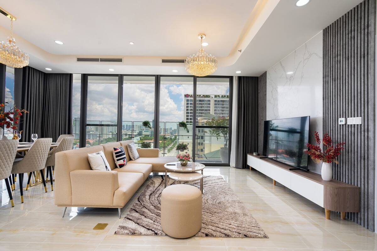 A modern living room with a sofa, ottoman, and coffee table, a TV, and a balcony with a city view.