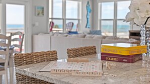 A Scrabble board game set on a marble table with a view of the ocean through large windows.