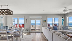 A spacious living area with a large window overlooking the beach, a dining area with a table set for four, and a cozy seating area with a sofa and chairs.