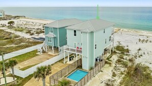 A two-story beachfront house with a swimming pool, a covered patio, and a beach view.