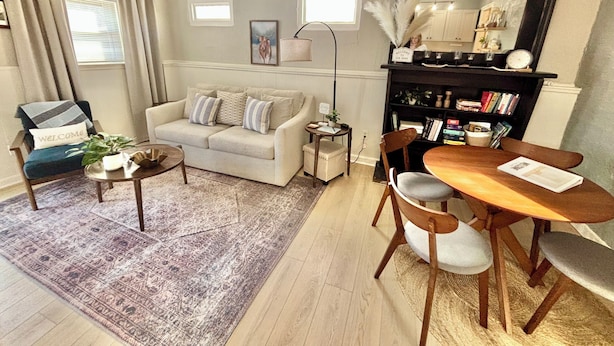 A living room with a sofa, coffee table, dining table, chairs, a bookshelf, and a mirror.