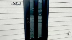 A black door with a glass panel, a mailbox with the number 7321/2, and a doormat with the text "so happy you're here."