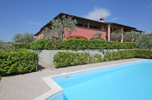 A building with a swimming pool, surrounded by greenery and a clear sky. - A House Among the Olive Trees - A Relaxing Vacation by the Lake. (Lombardia)