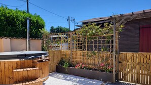 A patio area with a wooden barbecue grill, a seating bench, and a garden bed with flowers. - 3 Peaceful Country Gites - Sleeps 16 with 2 Wood-Fired Hot Tubs & Swimming Pool (Melle)