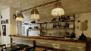 A rustic bar area with wooden furniture, hanging wicker lamps, and shelves with bottles and glasses. - A Stare [Stone Apartment - Historic Center - Molfetta] (Molfetta)