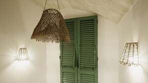 A room with a green shutter door, a woven light fixture, and a small wall-mounted object. - A Stare [Stone Apartment - Historic Center - Molfetta] (Molfetta)