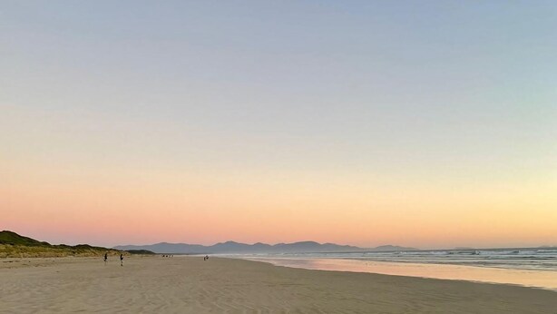 Una playa extensa con olas suaves y cielo despejado.
