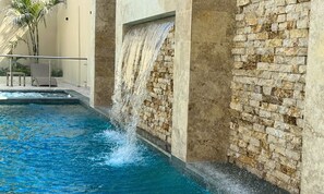 A pool with a waterfall feature, a stone wall, and a palm tree. - Cabañas Covemar (Coveñas)