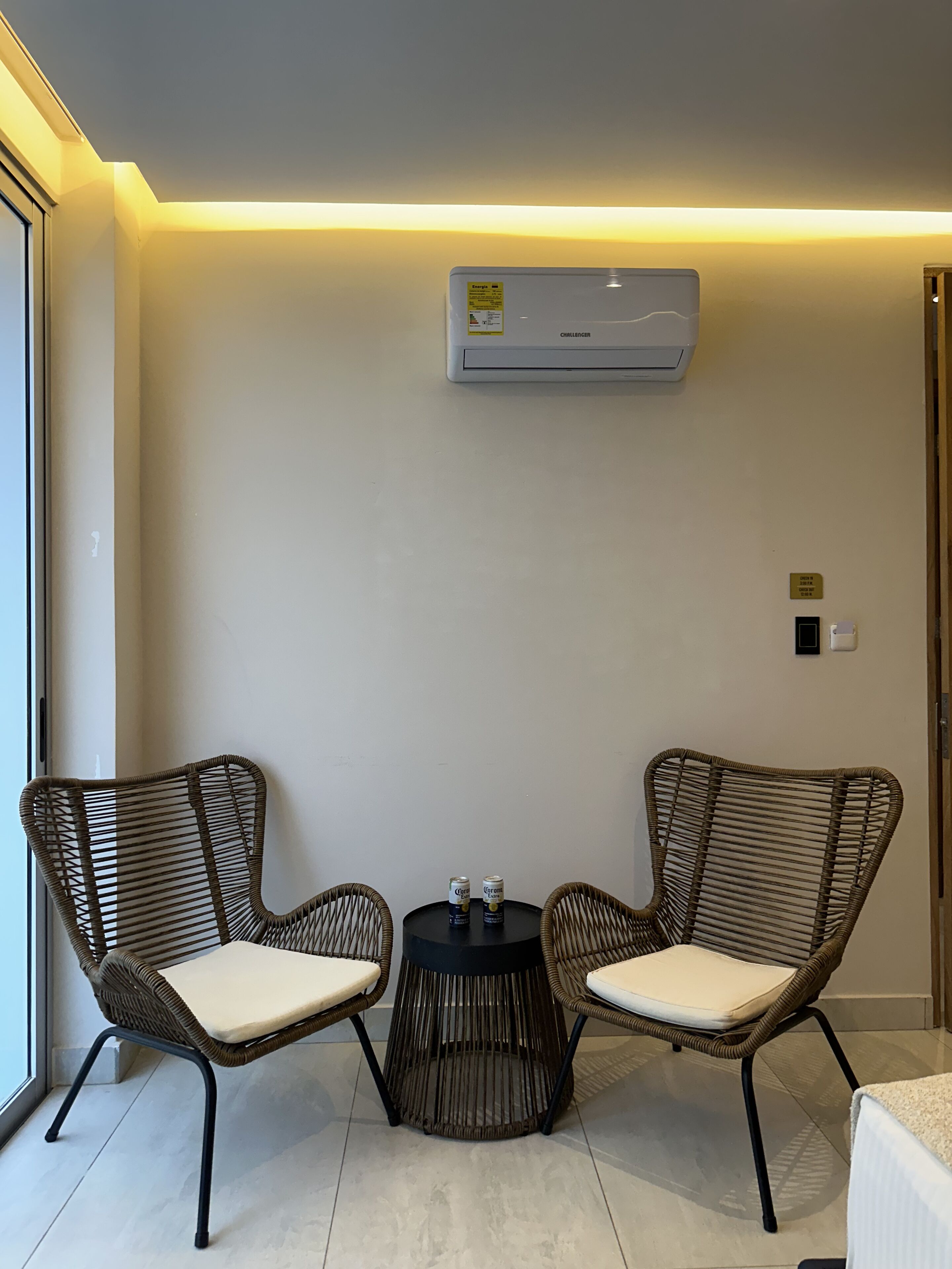 Une pièce comprenant deux fauteuils en osier, une petite table ronde et un appareil de climatisation fixé au mur.