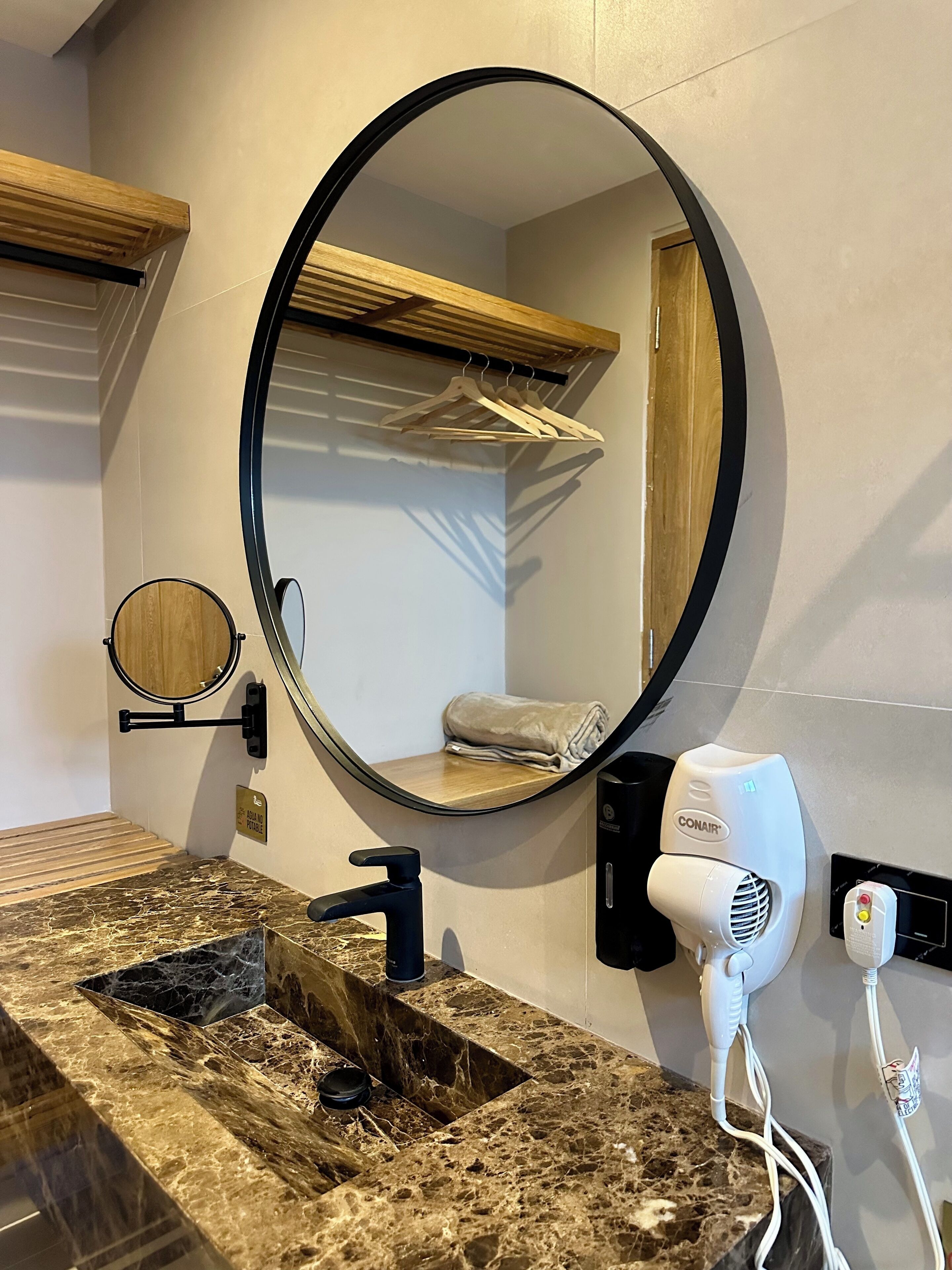 A bathroom with a marble sink, a round mirror, a towel rack, and a hairdryer.