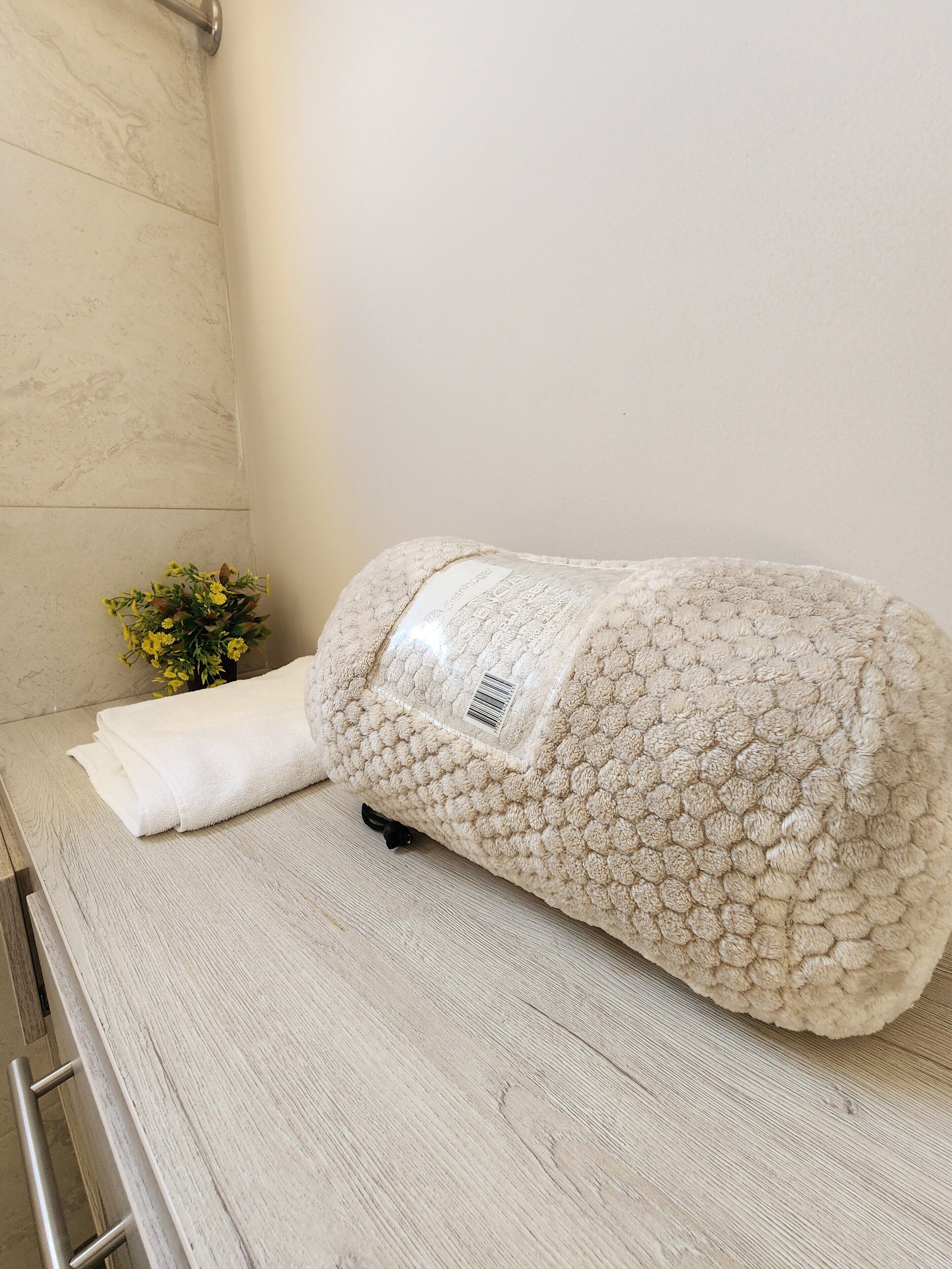 Un bagno con una parete rivestita di piastrelle color beige, un asciugamano bianco e un tappetino da bagno beige e soffice.