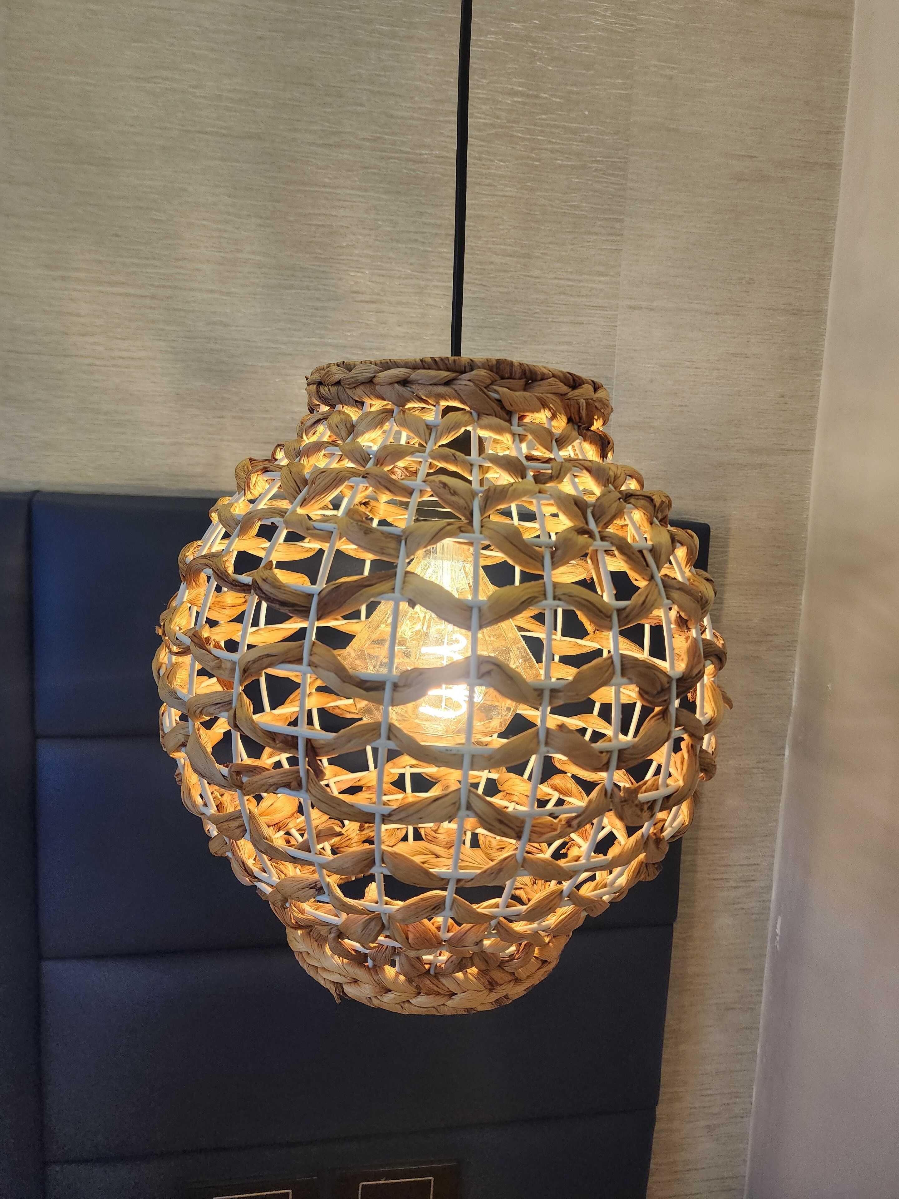 A woven pendant light fixture with a geometric pattern, hanging from a black cord.