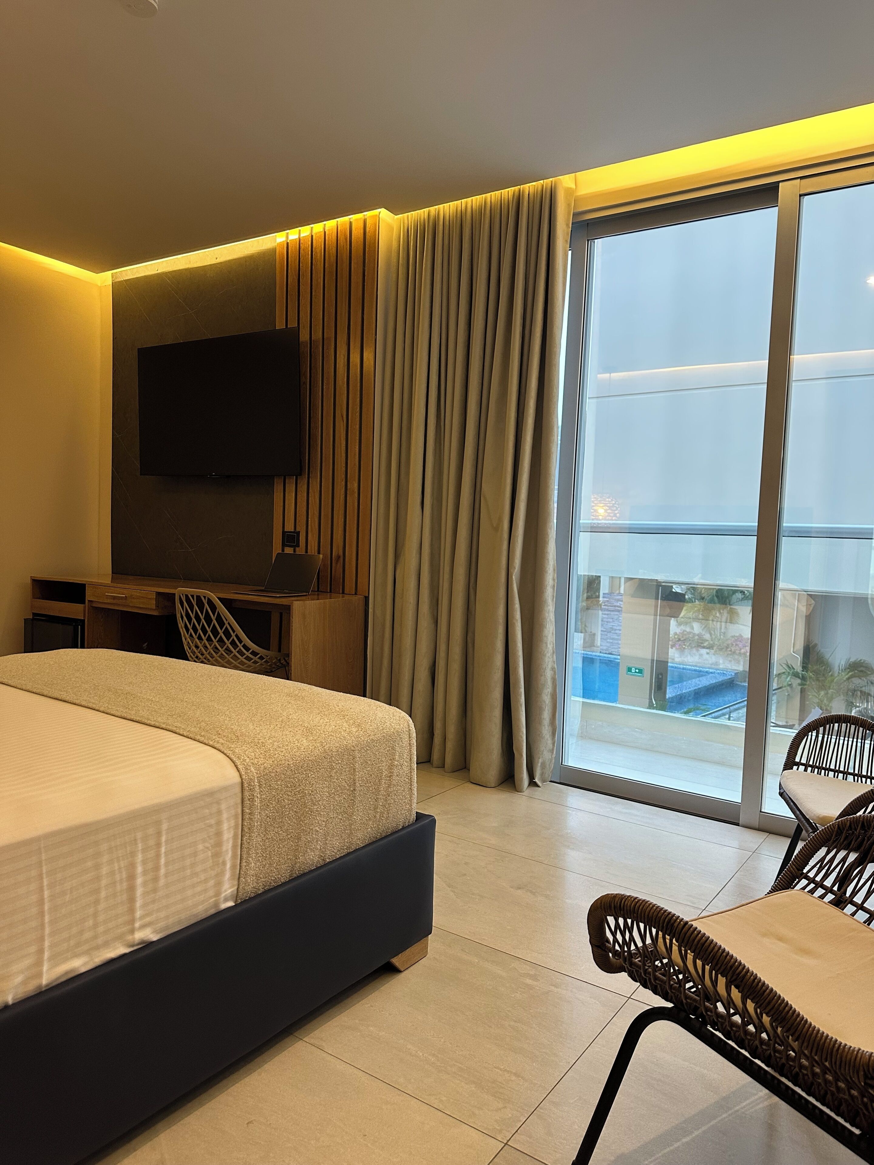 Una habitación de hotel moderna con una cama grande, un televisor de pantalla plana montado en la pared, un escritorio con una silla y un balcón con vistas.