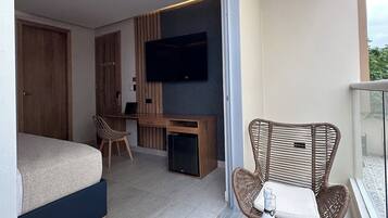 A modern hotel room with a bed, a desk, a TV, and a balcony with wicker furniture.