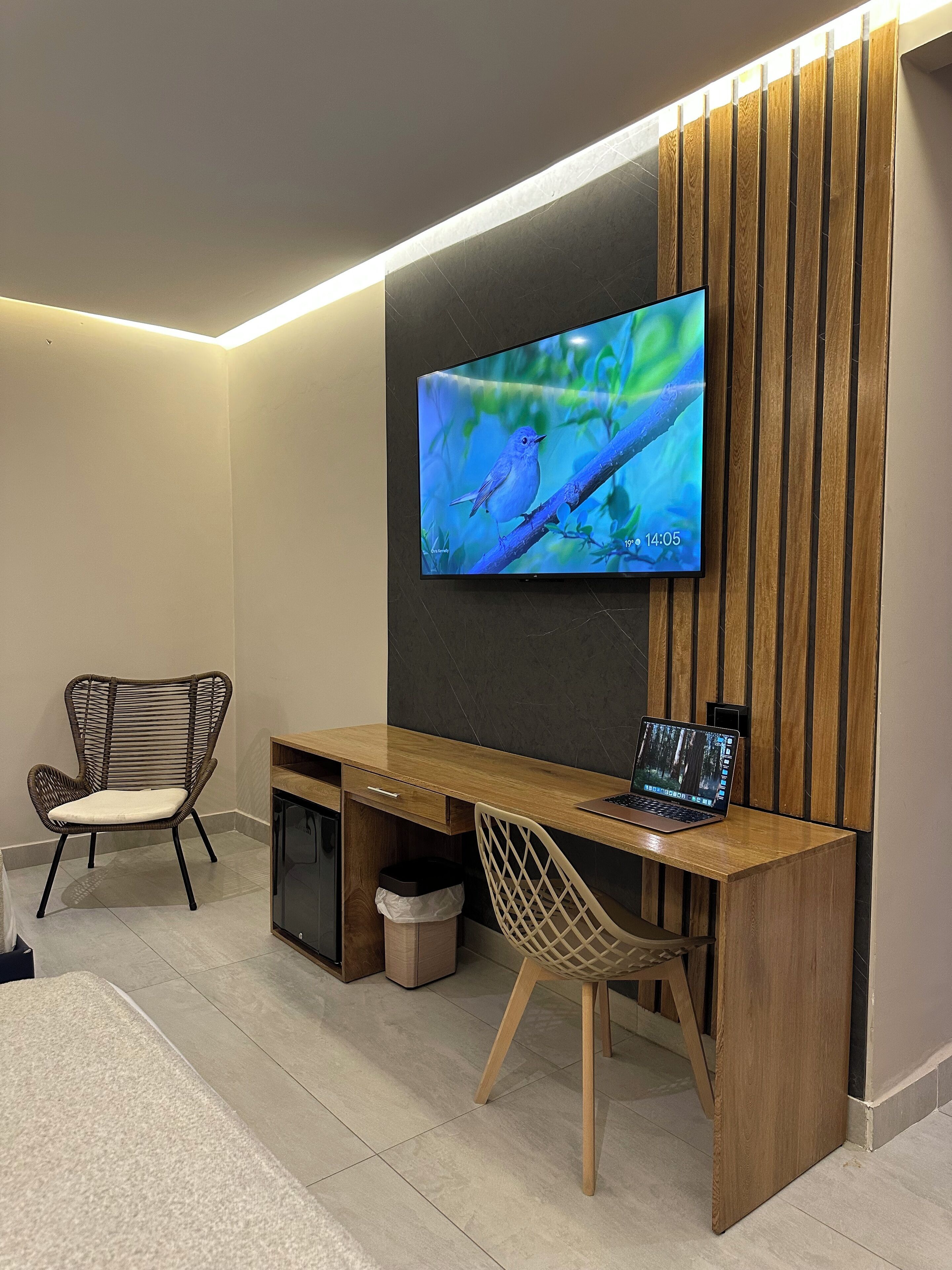A modern home office with a flat-screen TV mounted on a wooden wall, a wooden desk, two chairs, and a laptop.