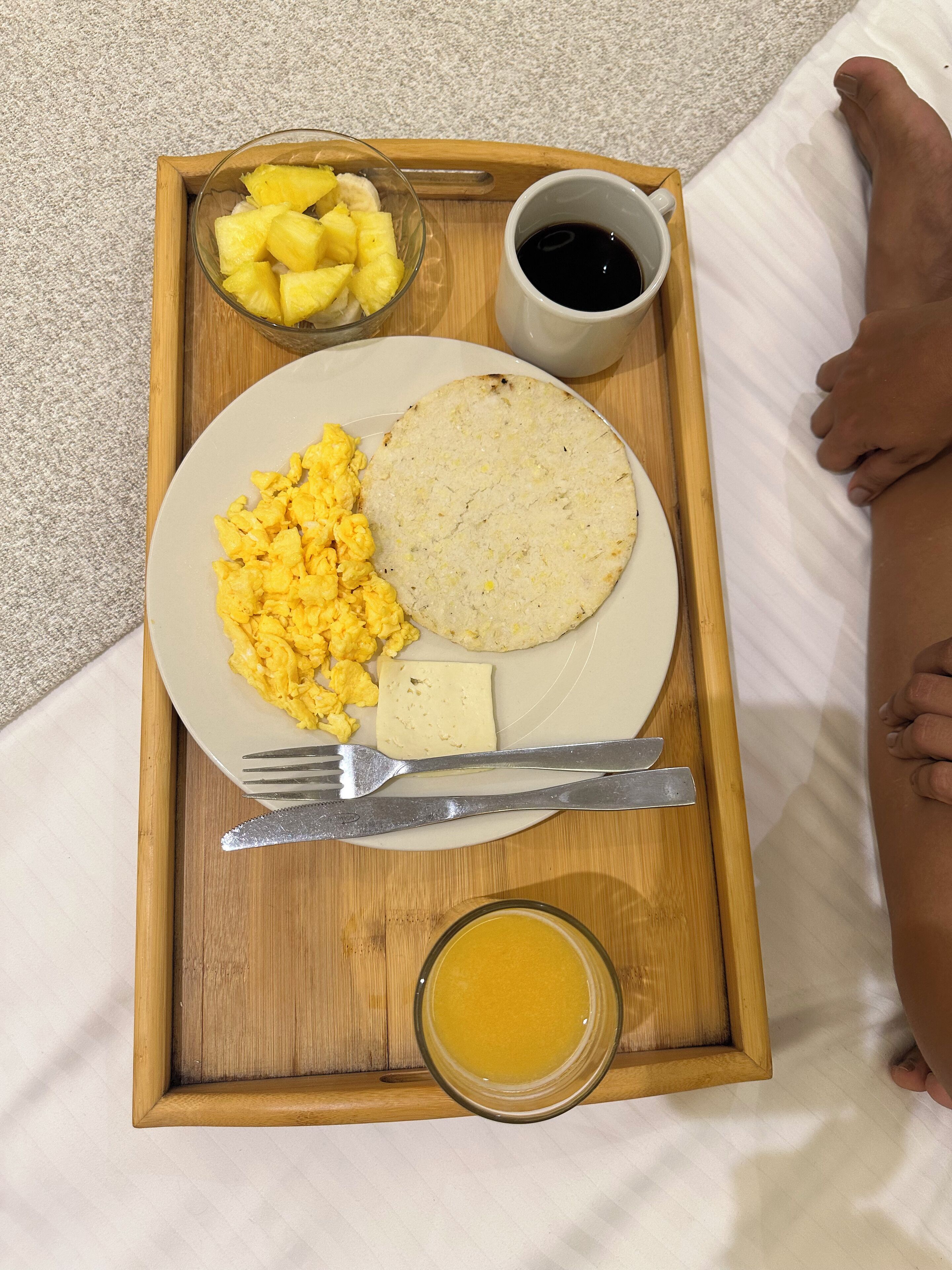 A wooden tray with breakfast items including scrambled eggs, a tortilla, pineapple chunks, and a cup of coffee.