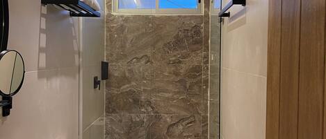 Een moderne badkamer met een marmeren douche, toilet en een wastafel met spiegel.