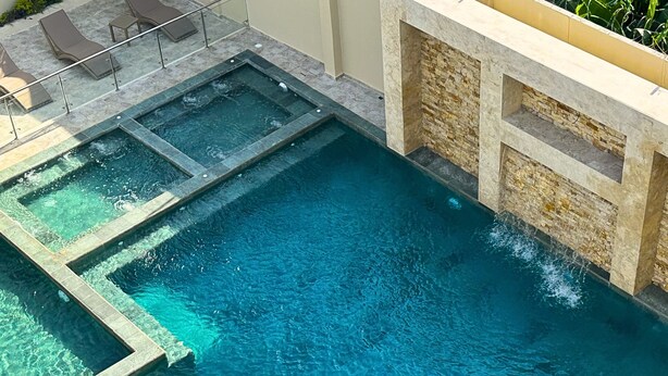 A rectangular swimming pool with clear water, surrounded by a stone wall and a tiled deck with lounge chairs. - Cabañas Covemar (Coveñas)