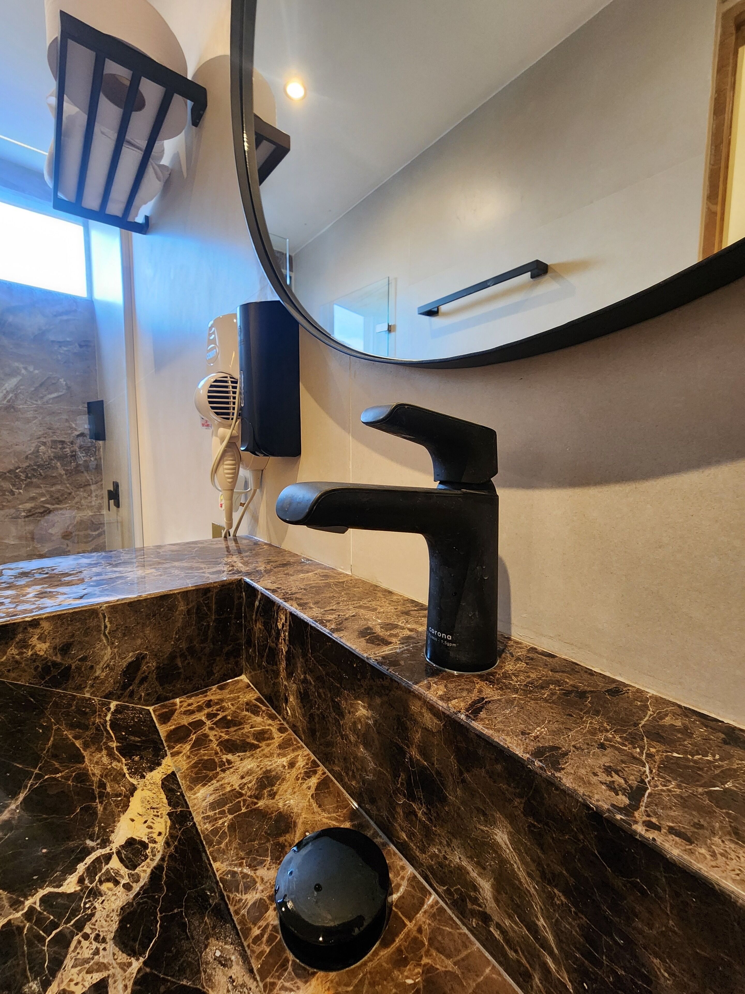 A bathroom with a black faucet, a marble countertop, and a round mirror.