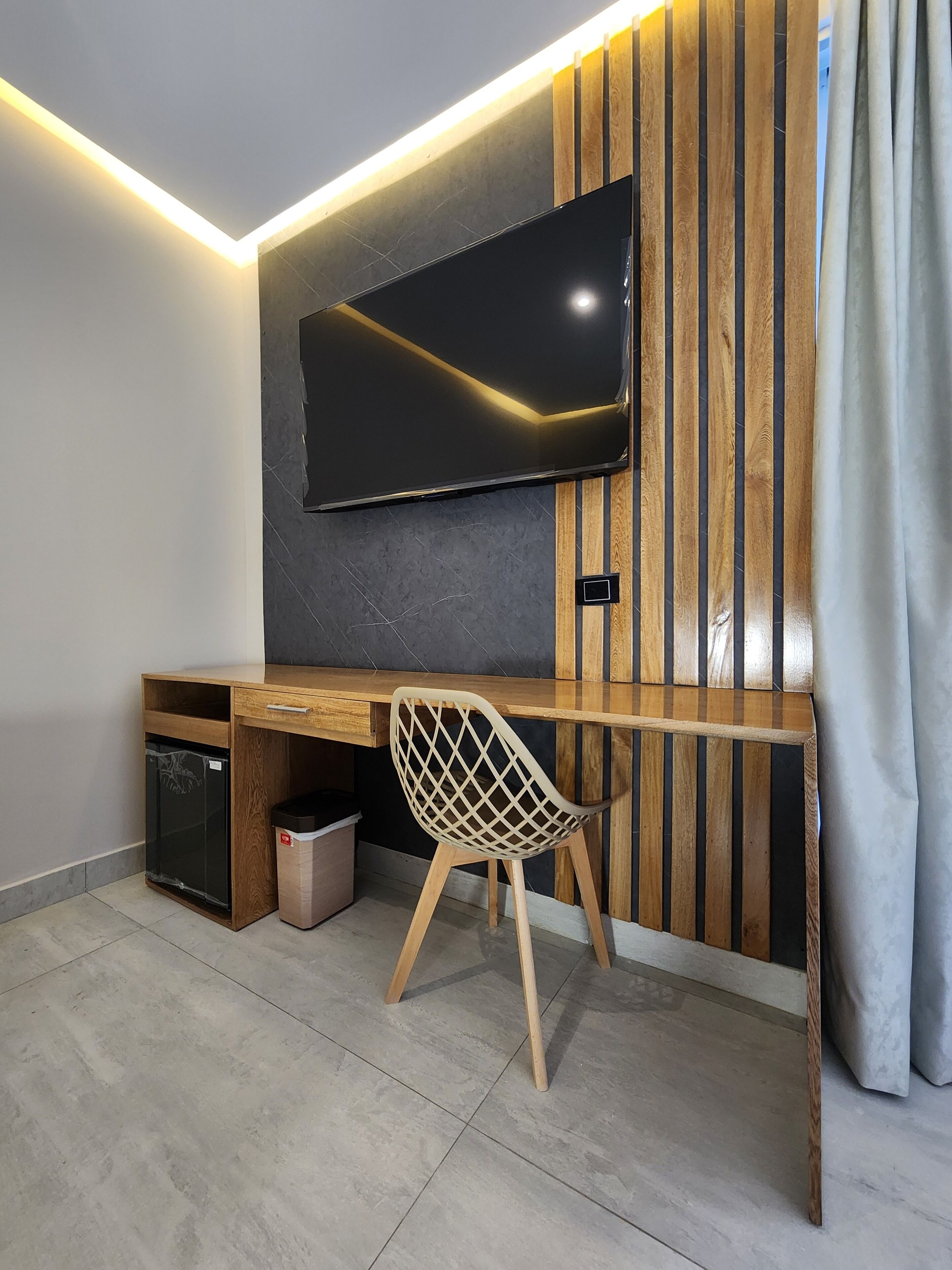 A modern room with a wooden desk, a TV mounted on the wall, a chair, and a small trash bin.
