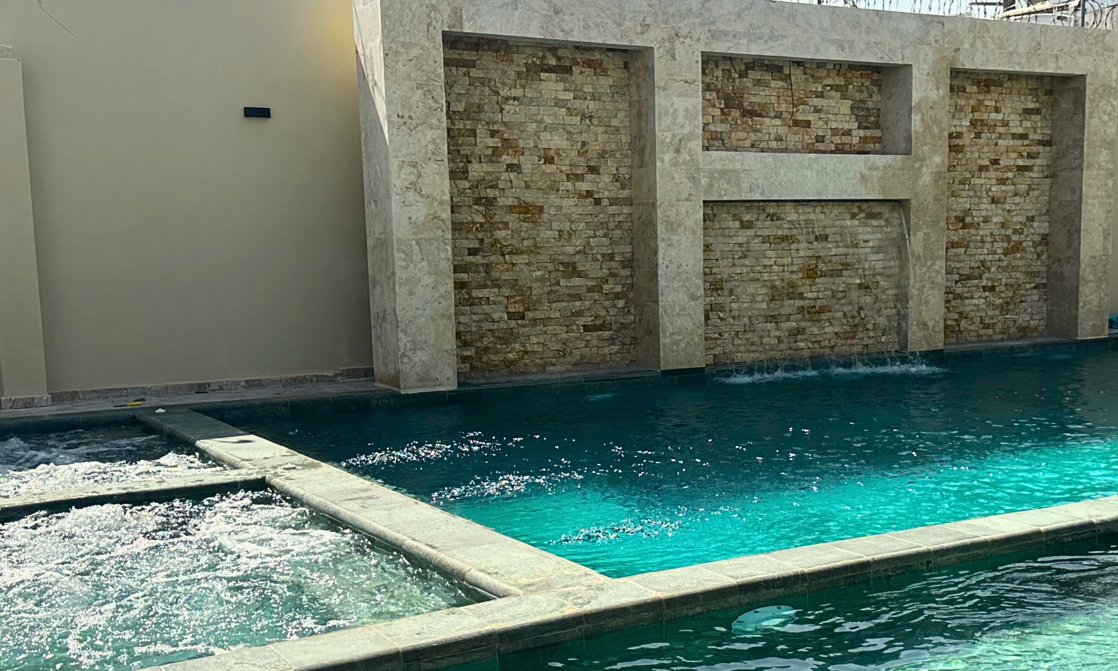 A swimming pool with a stone wall and a clear blue water feature.