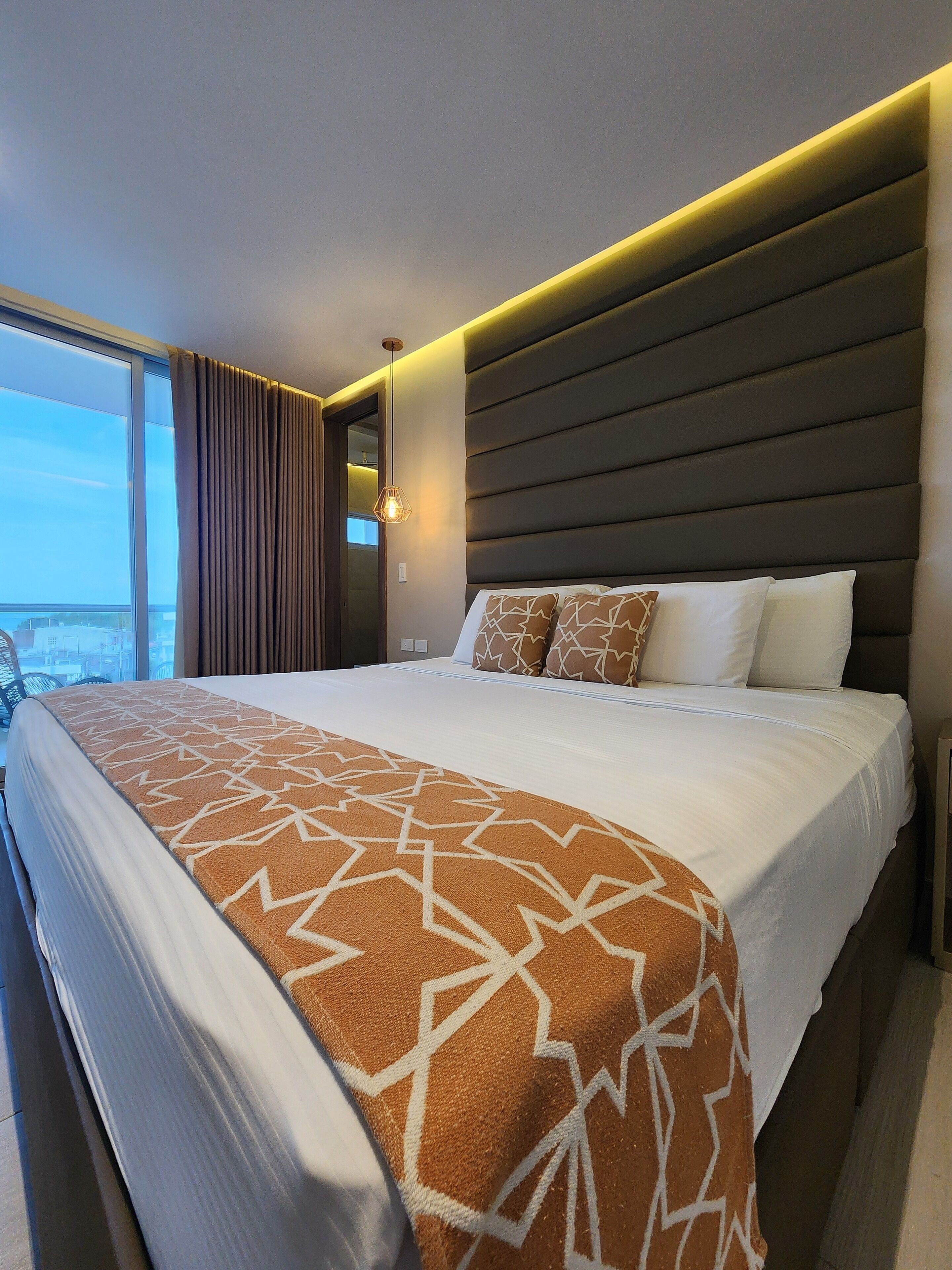 A modern hotel room with a large bed, a city view, and a unique geometric-patterned throw blanket.