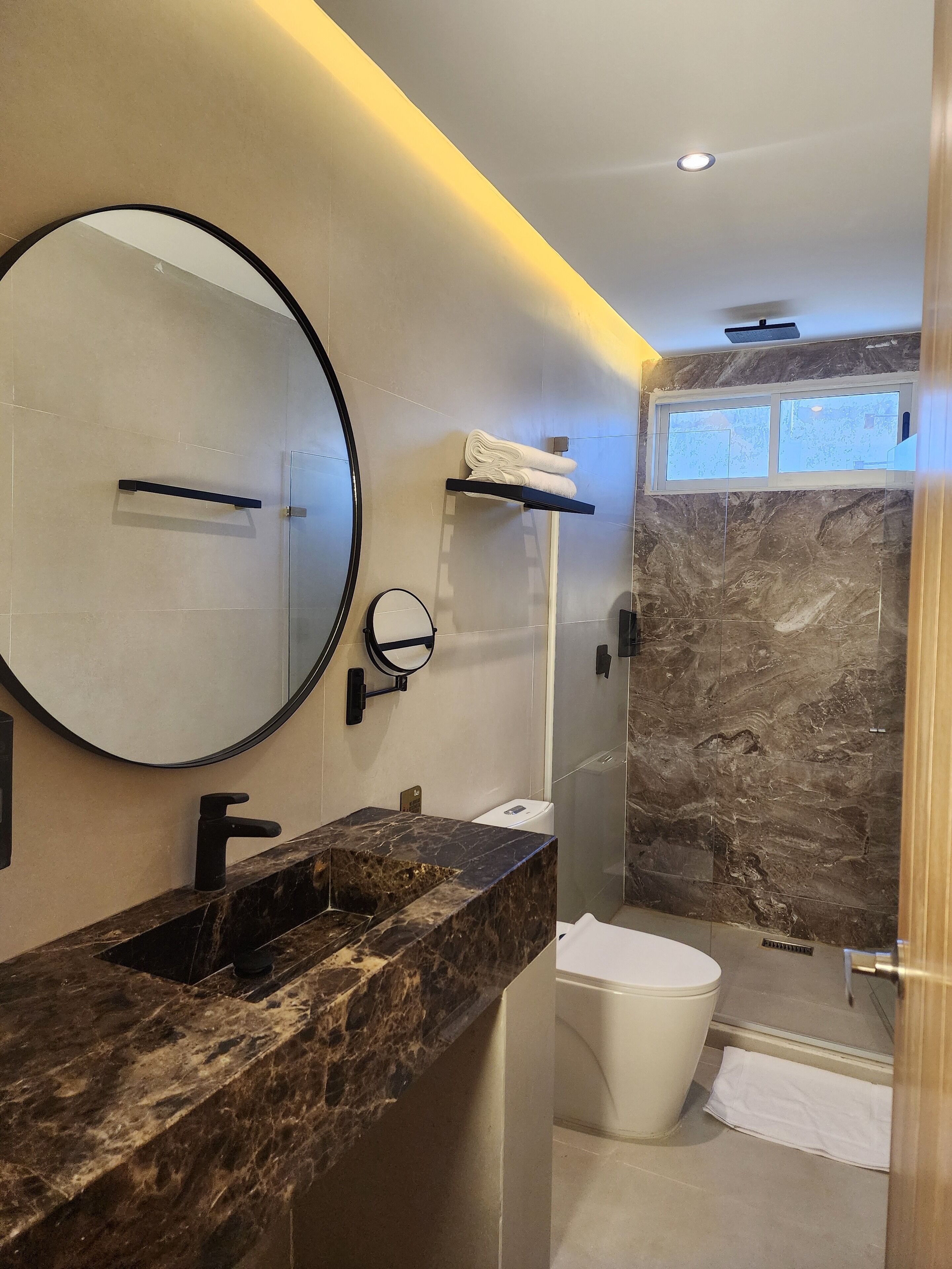 A modern bathroom with a marble sink, a large mirror, a towel rack, and a shower enclosure.