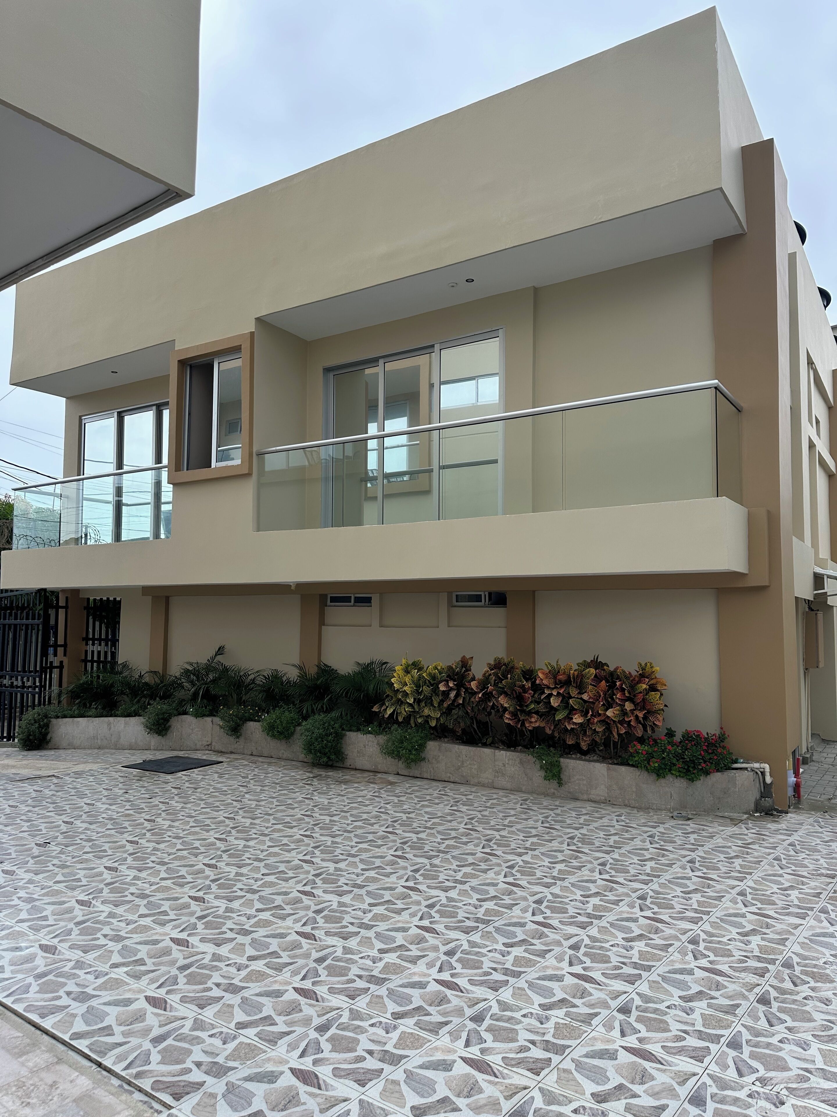 Um edifício moderno de dois andares com telhado plano, grandes janelas e varanda com guarda-corpo de vidro.