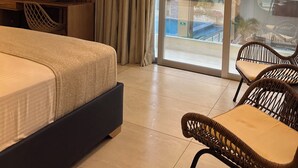 A hotel room with a bed, a TV, a desk, and a balcony with wicker chairs. - Cabañas Covemar (Coveñas)