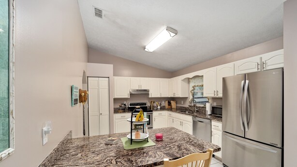 A kitchen with a marble countertop, white cabinets, a stainless steel refrigerator, and a two-tiered fruit stand. - Nellies Cottage is 4 miles from WEC-World Equestrian Center (Ocala)